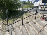 Ett handräcke i metall vid en betongtrappa som leder upp till en trottoar.